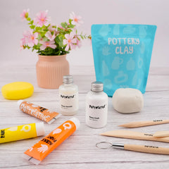 A close-up of the Pottreative air dry clay kit materials, featuring clay, base coat, gloss varnish, acrylic paints, and wooden sculpting tools.
