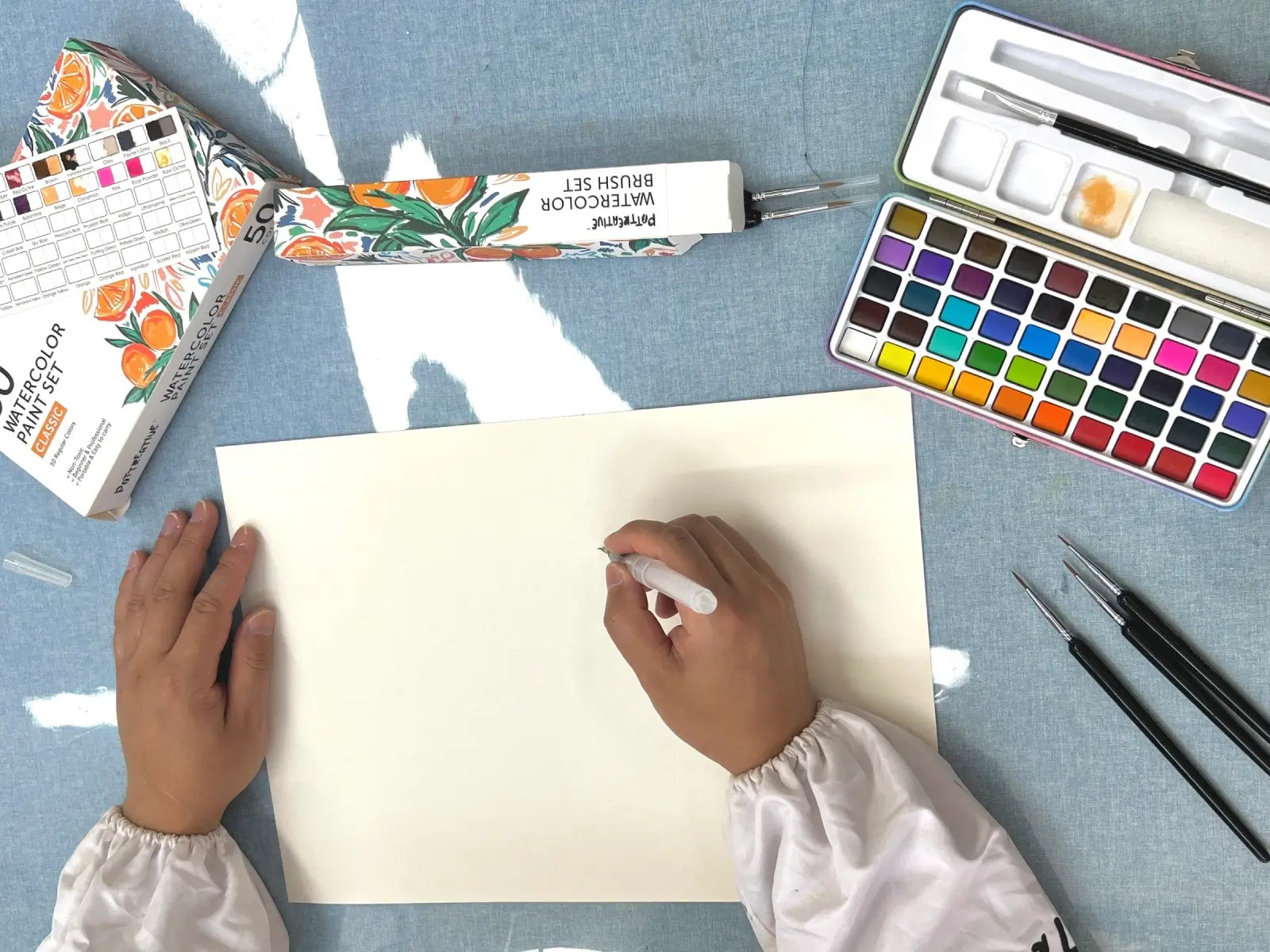 A person preparing to paint with a watercolor set and brushes.
