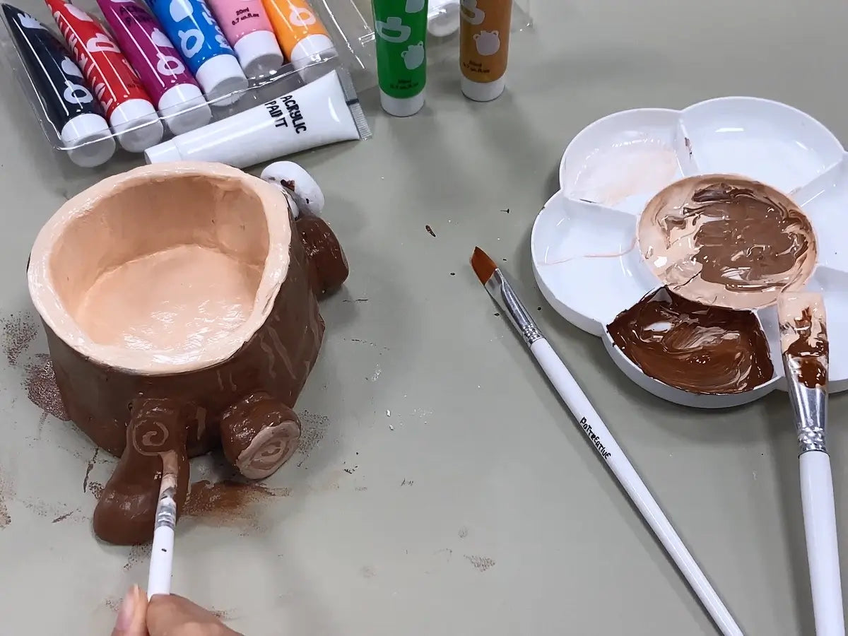 A person painting a brown clay sculpture with a brush.