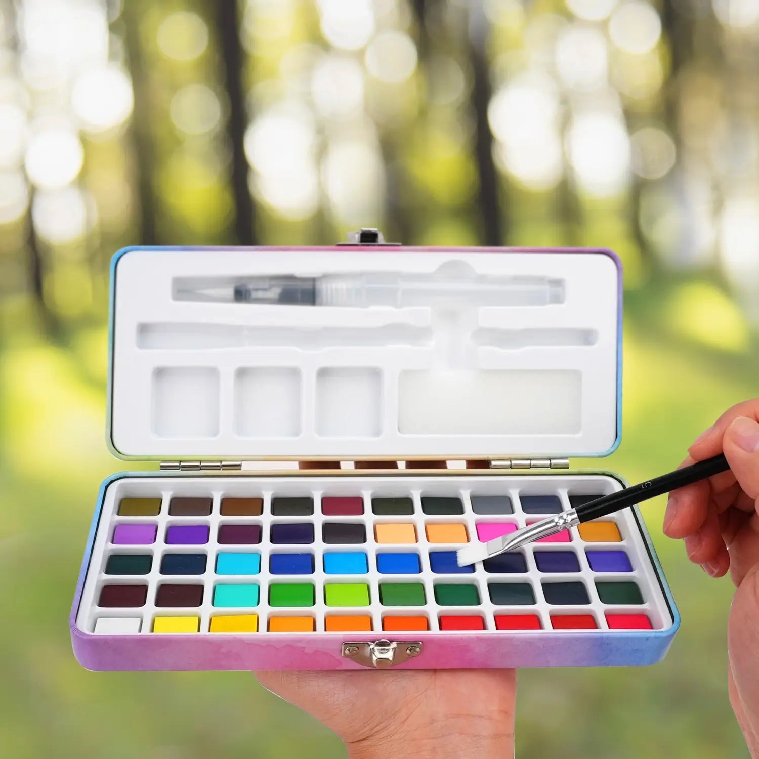A person holds the open 50 colors watercolor paint set outdoors. A perfect portable travel kit for painting anywhere.